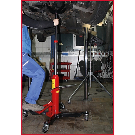 Ein Mechaniker hebt ein Auto mit einer roten Hebebühne an. Das Auto ist teilweise sichtbar.